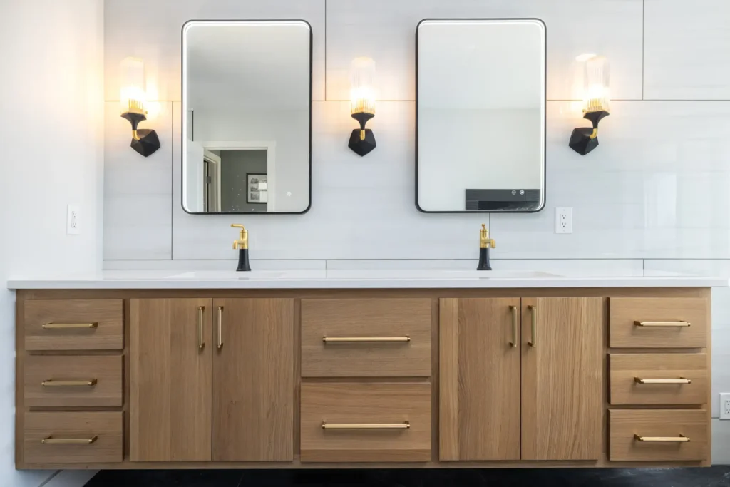 Double vanity bathroom with wooden cabinets, brass hardware, and two large mirrors. Modern light fixtures and sleek black and gold faucets add a stylish touch.