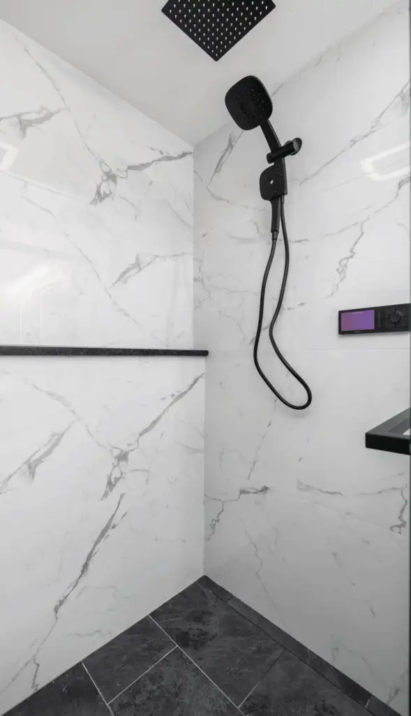 Modern bathroom shower with white marble walls featuring gray veining, complemented by a matte black overhead and handheld shower system, with a built-in shelf and contrasting dark floor tiles.