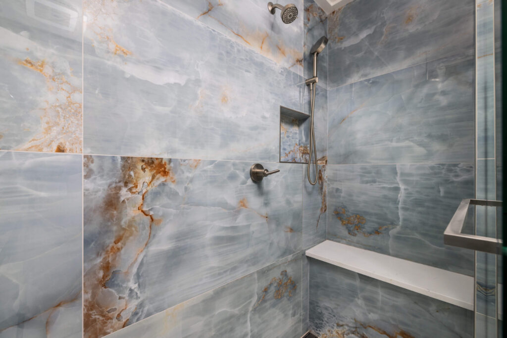 Luxurious shower with stunning blue and gold marble tiles, featuring a sleek rainfall showerhead and a built-in bench for comfort. The tiles create an elegant and opulent atmosphere.