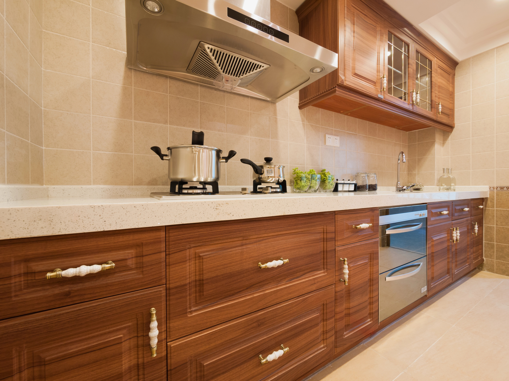 Modern kitchen with wooden cabinets, stainless steel appliances, a range hood, and pots on the countertop against a beige tiled wall.